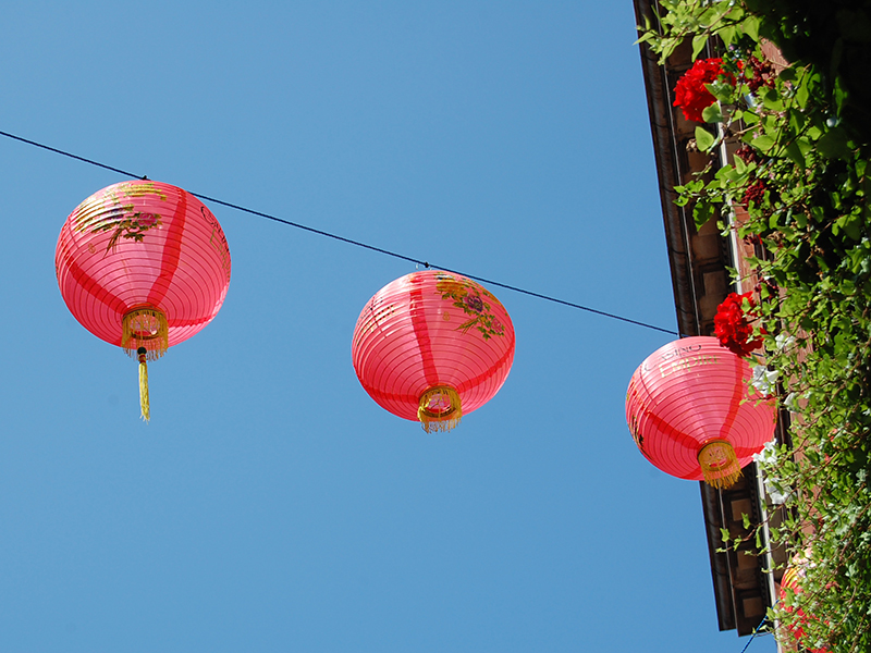 Aus der Froschperspektive fotografierte rote, chinesische Lampions vor blauem Himmel.