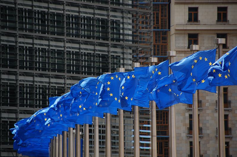 Mehrere EU-Flaggen wehen an Fahnenmästen, im Hintergund ein Gebäude der EU-Kommission in Brüssel.