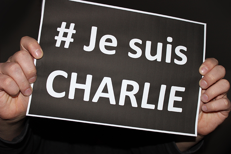 Jemand hält ein schwarzes Schild mit der weißen Aufschrift "#Je suis Charlie" hoch.