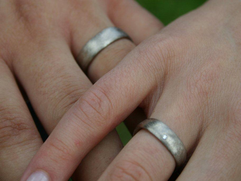 Detailaufnahme der Hände eines Brautpaares mit den silbernen Eheringen am Ringfinger.