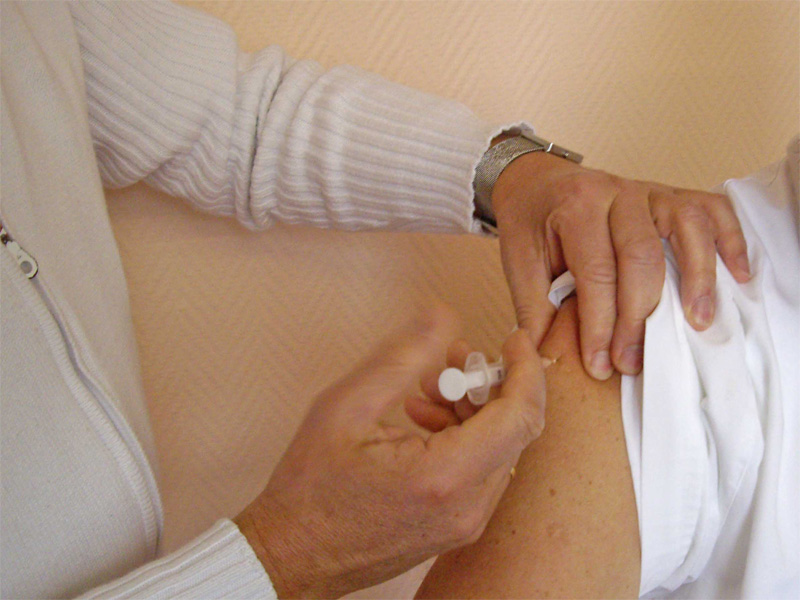 Impfung: der Bildausschnitt zeigt einen Mediziner, der einem Patienten eine Spritze in den Oberarm verabreicht.