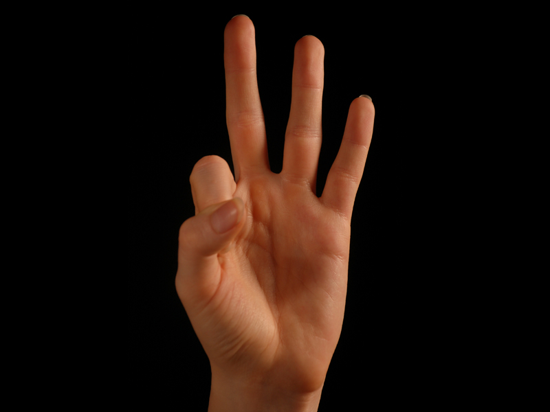Hand vor schwarzem Hintergrund, die die Gebährde für "gut" formt: Zeugefinger und Daumen zu einem Kreis geformt, Mittel-, Ring- und kleiner Finger sind abgespreizt