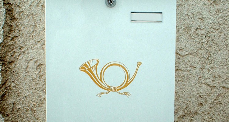 Bild eines weißen Briefkastens mit goldenem Posthorn darauf an einer Hauswand.
