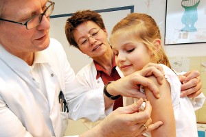 Ein Kinderarzt verabreicht einem jungen Mädchen eine Impfung in den Oberarm, eine Ärztin sieht dabei zu.