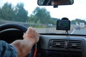 Blick vom Rücksitz in die Auto-Fahrerkabine auf den Arm des Fahrers am Lenkrad und das Navigationsgerät an der Windschutzscheibe.