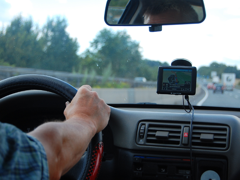 Blick vom Rücksitz in die Auto-Fahrerkabine auf den Arm des Fahrers am Lenkrad und das Navigationsgerät an der Windschutzscheibe.