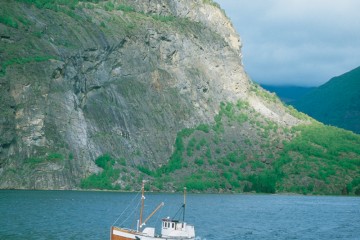 Ein Schiff fährt über das Meer, im Hintergrund große, teilweise bewachsene Felsen.