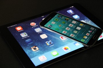 Vor dunklem Hintergrund liegen ein Tablet und darsuf ein Smartphone, auf beiden Geräten sind verschiedene Apps zu sehen.