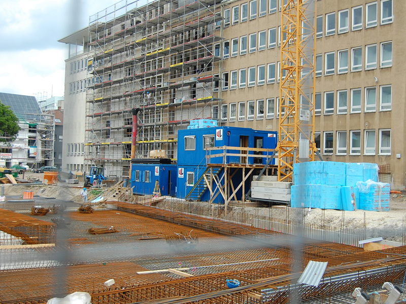 Blick durch einen Bauzaun auf eine Baustelle an einem großem Gebäude.