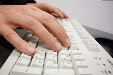 Nahaufnahme der Hände eines Mannes an einer hellgrauen Computer-Tastatur.