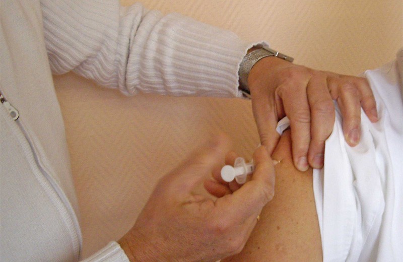 Impfung: der Bildausschnitt zeigt einen Mediziner, der einem Patienten eine Spritze in den Oberarm verabreicht.