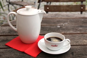 Bild eines weißen Kaffeekännchens und einer weißen Tasse, das Set steht auf einem rustikalen Holztisch.