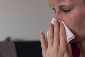 Eine junge Frau putzt sich mit einem Papiertaschentuch die Nase.