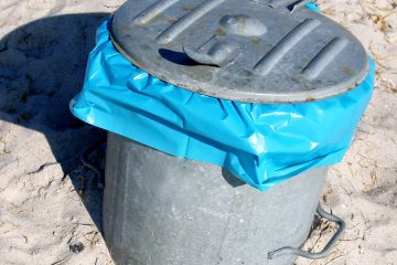 Nahaufnahme eines Blechmülleimers mit Deckel, unter dem eine blaue Mülltüte hervorragt.