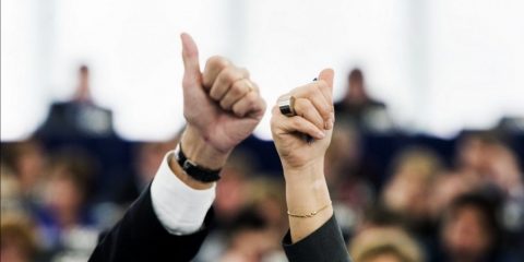 Nahaufnahme einer weiblichen und einer männlichen Hand, die mit dem Daumen nach oben zeigend im Parlament zur Abstimmung in die hochgehalten werden