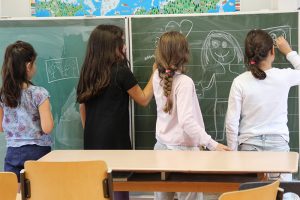 Vier Mädchen stehen an einer Tafel im Klassenzimmer und beschreiben und bemalen diese.